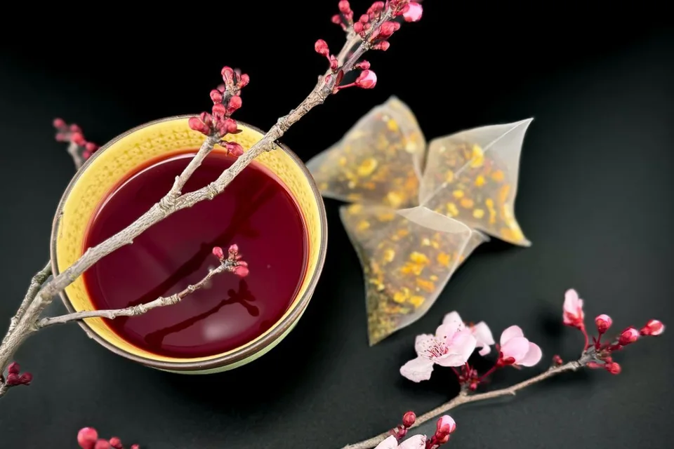 A cup of herbal tea with pink blossoms and tea sachets