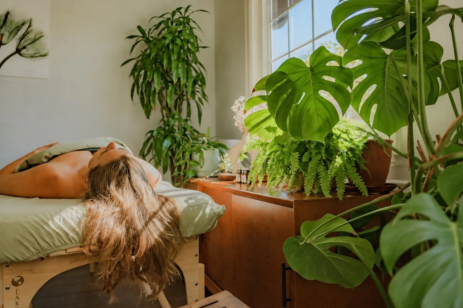 A patient resting in a sunlit treatment room surrounded by lush green plants