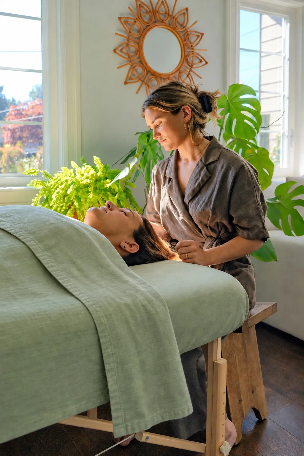 A patient resting on a massage table with her practitioner in a sunlit treatment room