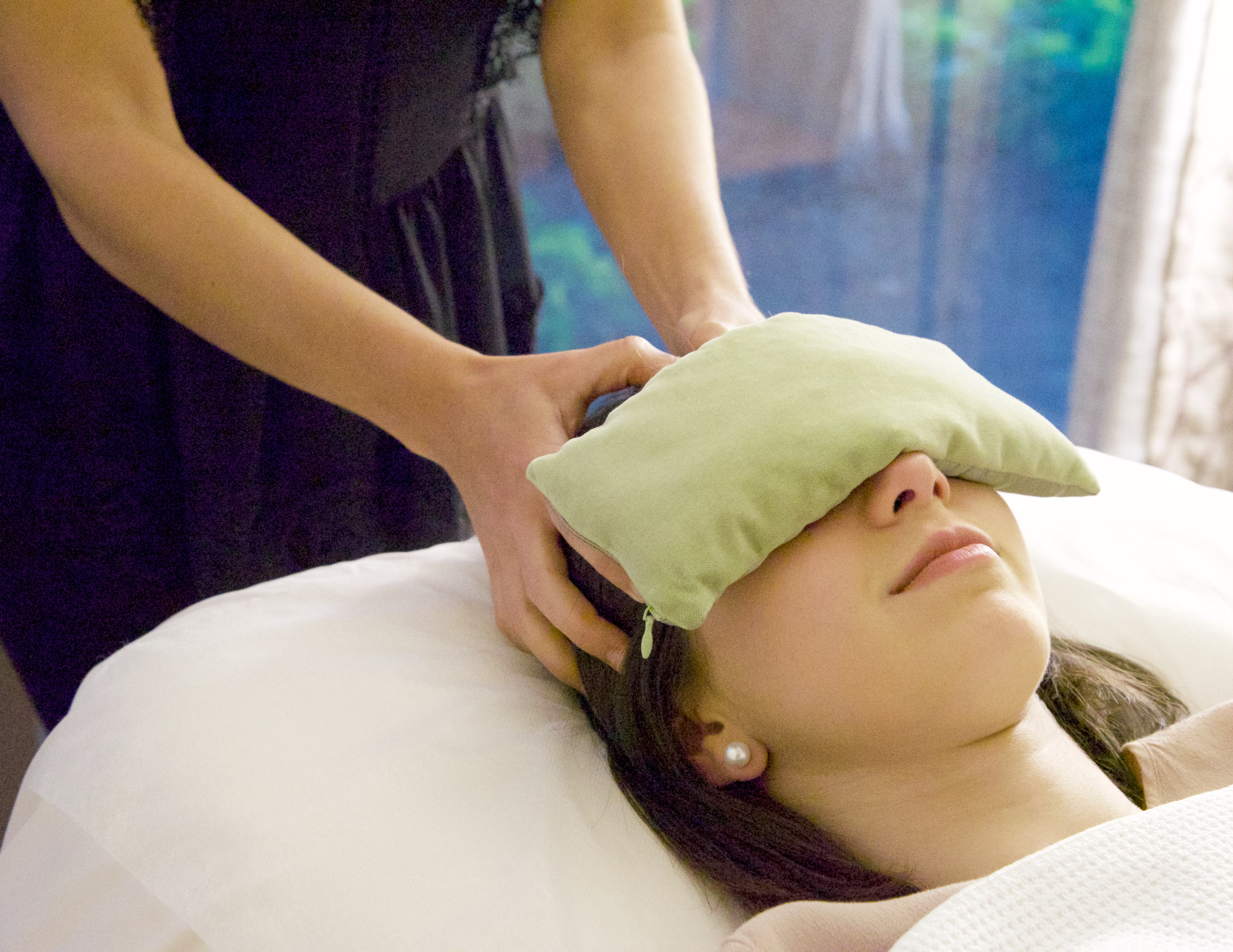 A patient resting with an eye pillow while receiving gentle head and neck massage