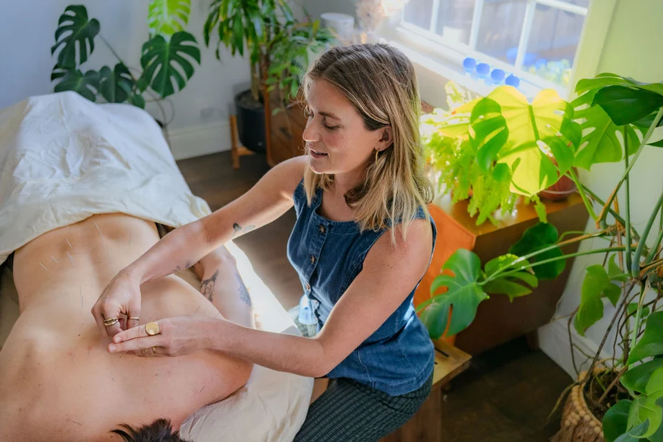 Taylar placing acupuncture needles in a patient’s back in a sunlit treatment room